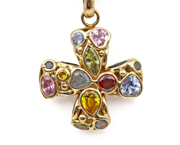 A 14 karat yellow gold, equal-armed cross with various semi-precious gemstones of different shapes and sizes bezel set into both faces of the pendant. The cross has a yellow gold o-ring bail that is shown with a rope chain threaded through it.
