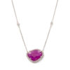 A 14 karat white gold necklace with small, bezel set diamond stations. At the center of the necklace is a freeform cut ruby with a diamond bezel.