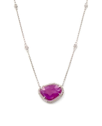 A 14 karat white gold necklace with small, bezel set diamond stations. At the center of the necklace is a freeform cut ruby with a diamond bezel.
