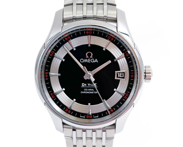 Omega DeVille stainless steel watch with round black dial that features an inner silvertoned ring. The watch has bars for markers, a date window at three o'clock, and a sweeping second hand. There are red indicators at the outside end of each bar marker, making it stand out against the black bezel ring.